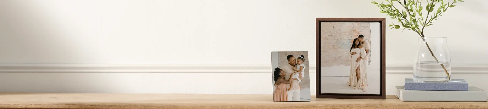 Wooden shelf with two framed photos, a vase with green leaves, and books; yellow 'A' circle above on the wall.