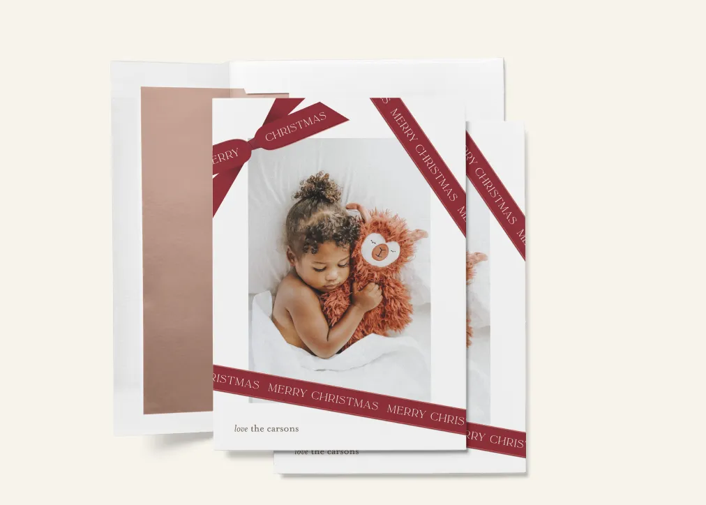 Christmas card featuring a child cuddling a plush toy with red ribbon design and “Merry Christmas” text.